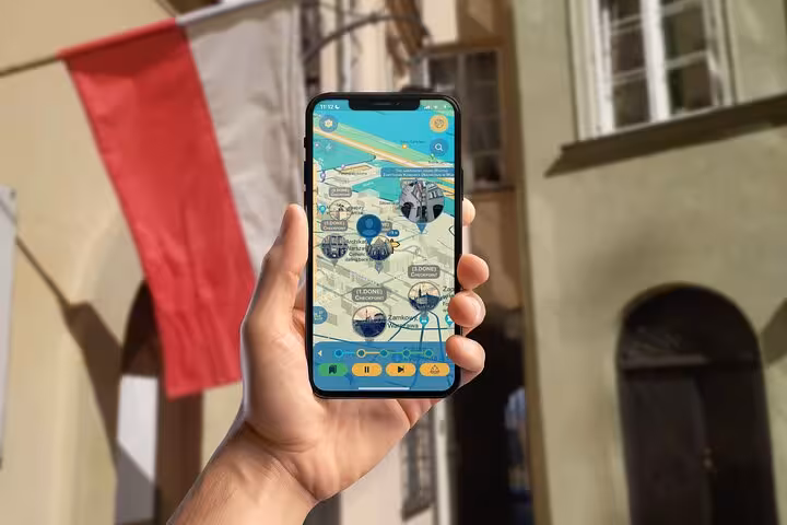 Hand holding smartphone displaying interactive map app for self-guided medieval Warsaw walking tour with Polish flag backdrop