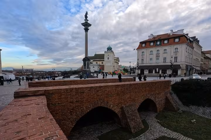 Hand holding a smartphone displaying a self-guided walking tour app map of Medieval Warsaw Old Town landmarks