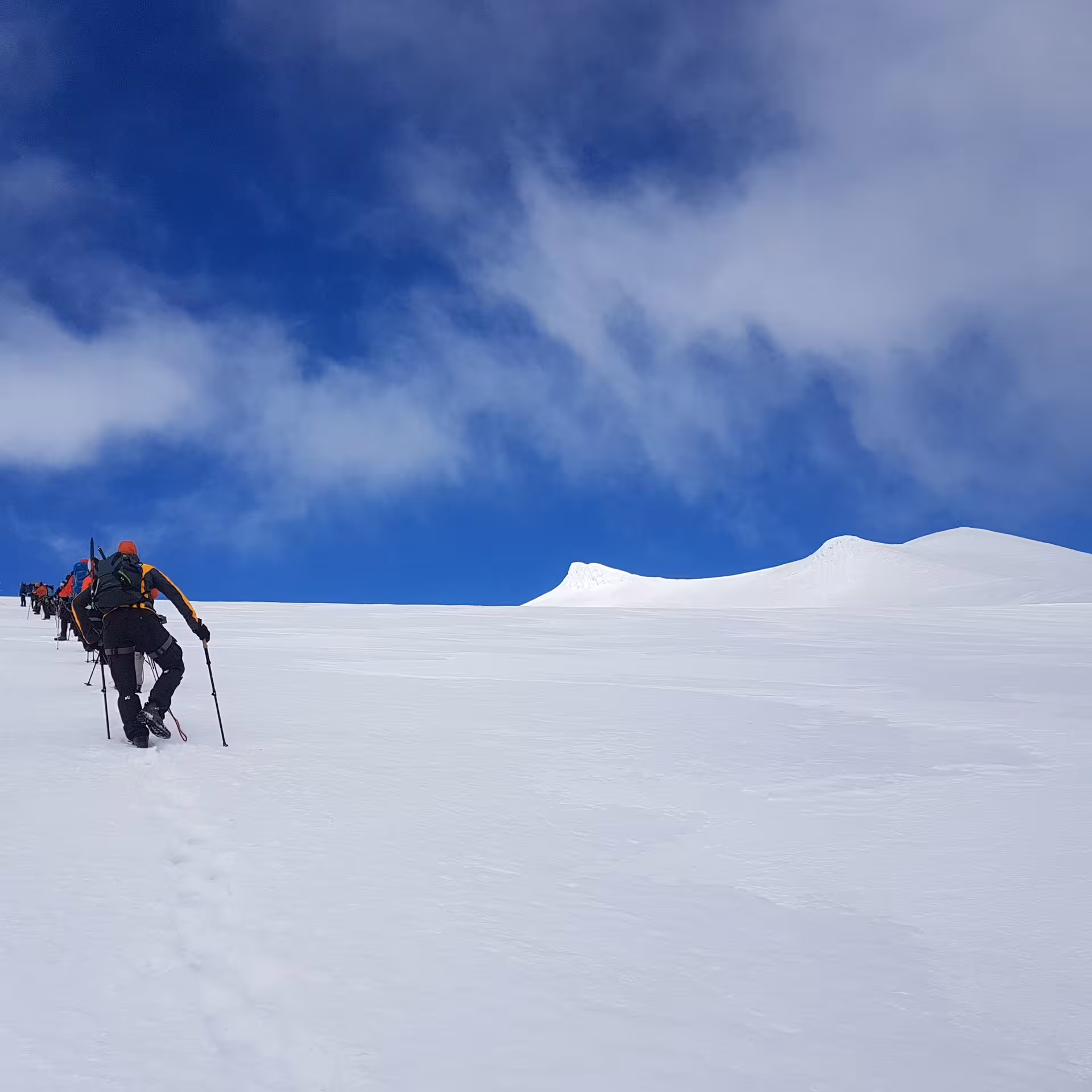 Group of hikers ascending Snaefellsjokull glacier in single file under dramatic blue sky