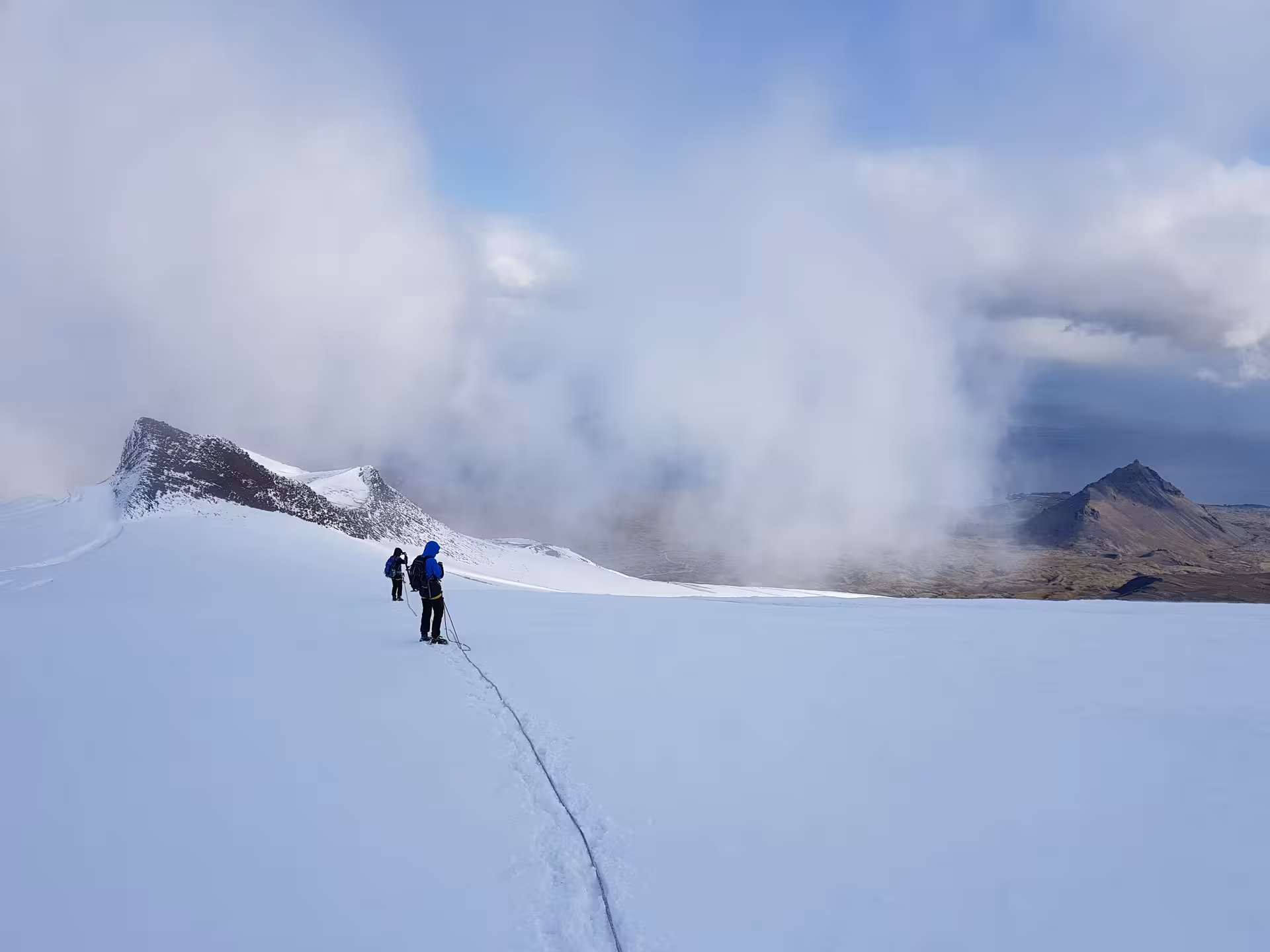 Two hikers roped together trekking across Snaefellsjokull glacier with dramatic clouds and mountain peaks