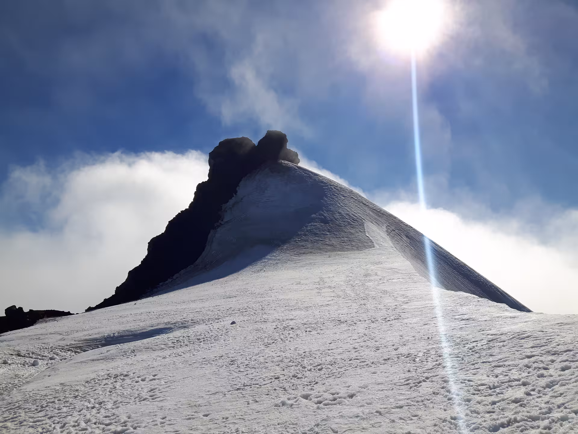 Snow-covered Snaefellsjokull glacier peak with dramatic sunburst and rocky summit under blue sky