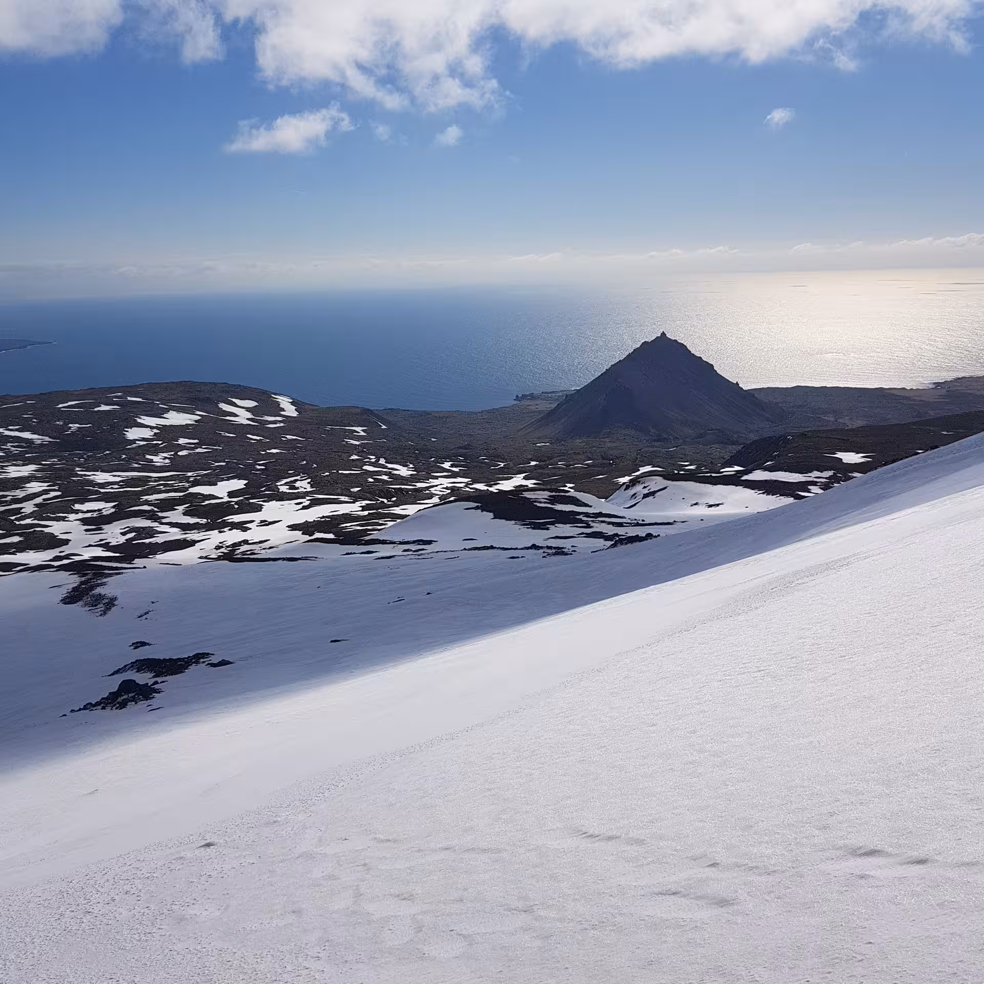 Snow-covered Snaefellsjokull glacier slope with volcanic peak and Atlantic Ocean in background, Iceland