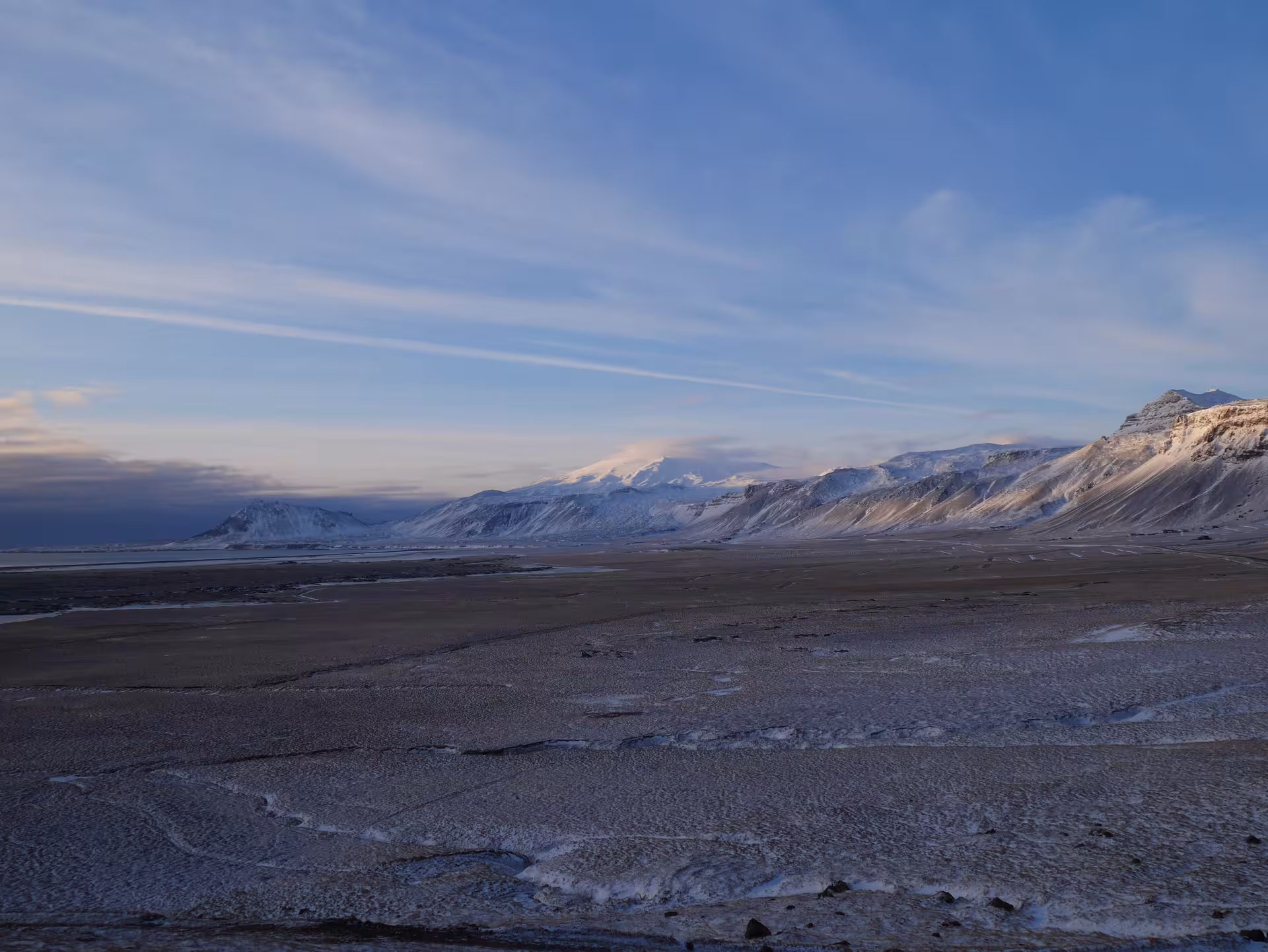 Snow-covered Snæfellsjökull glacier and volcanic mountains across a vast frozen lava plain in Iceland