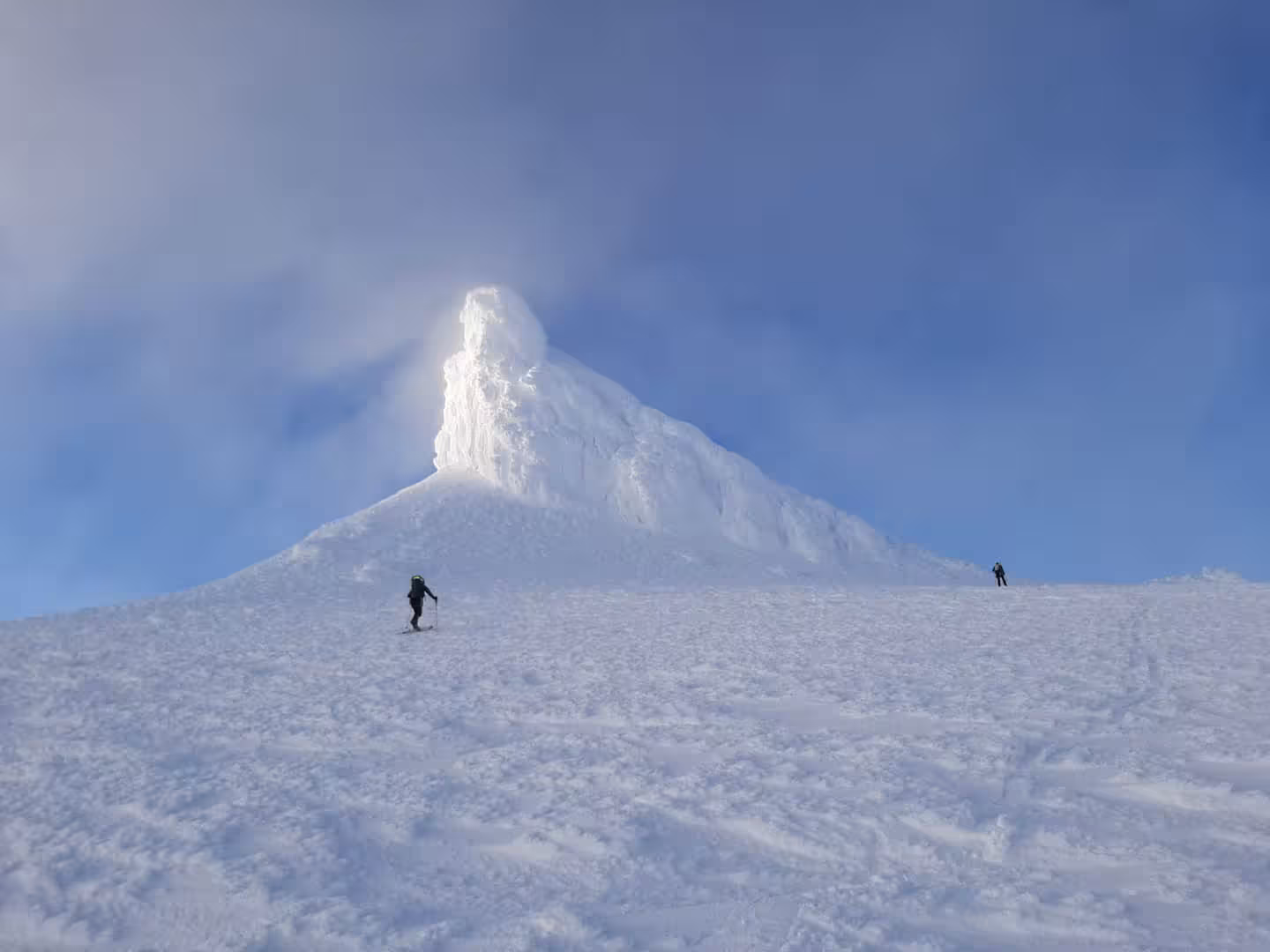 Two skiers ascending snow-covered Snaefellsjokull glacier with dramatic icy summit peak and blue sky