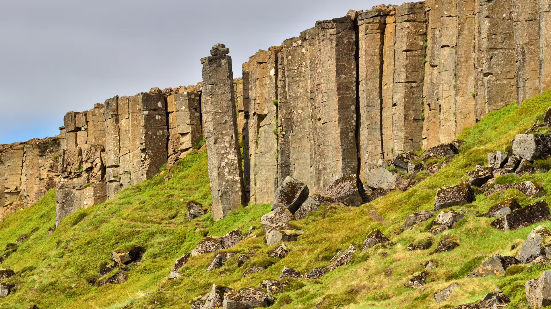 Tall basalt rock columns rising from a green grassy hillside on the Snaefellsnes Peninsula, Iceland