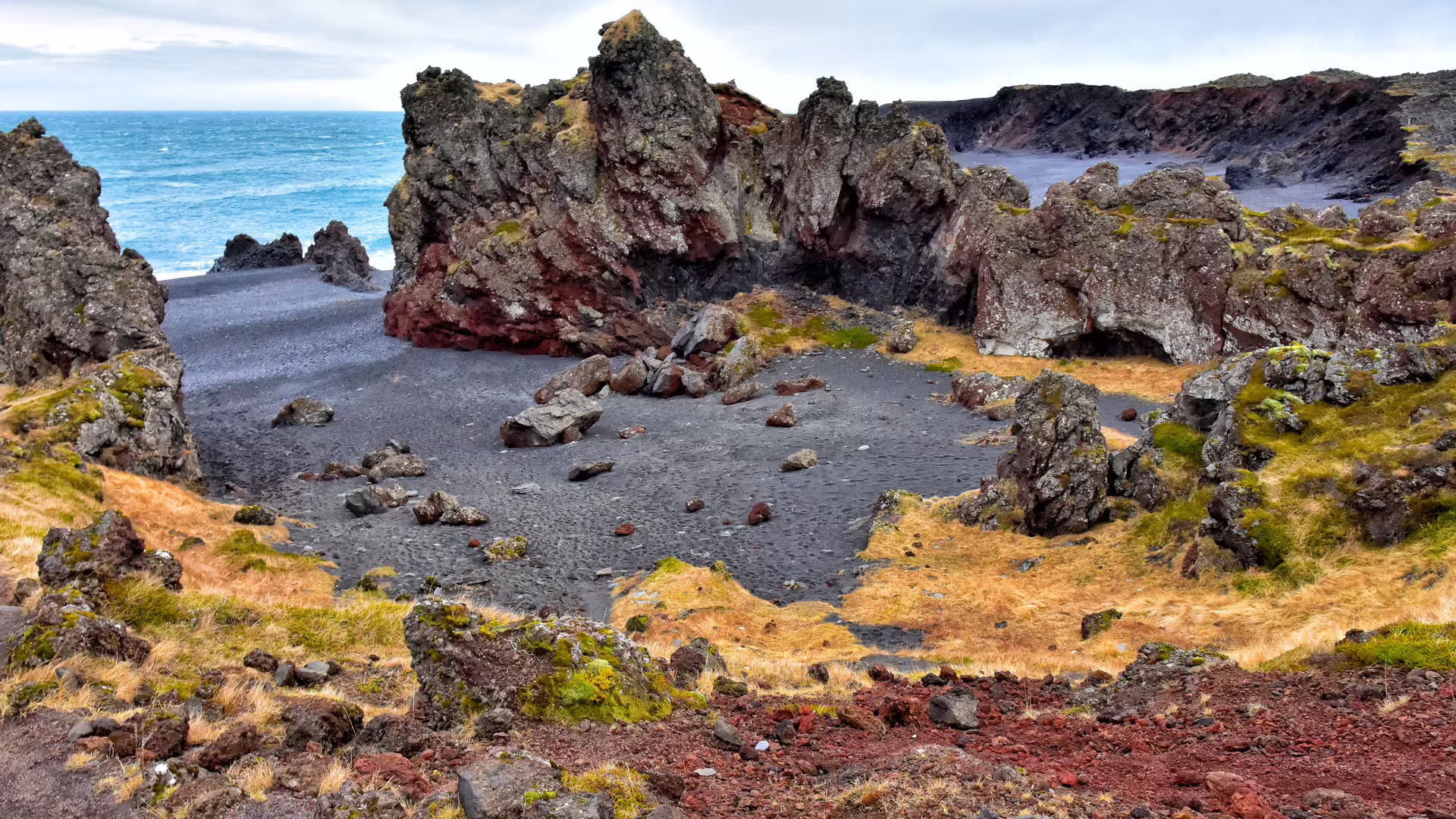 Black sand beach with dramatic lava rock formations and golden grass on Snaefellsnes Peninsula, Iceland