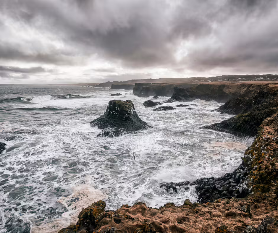 Dramatic rocky coastline with crashing waves and dark cliffs under stormy skies on Snaefellsnes Peninsula