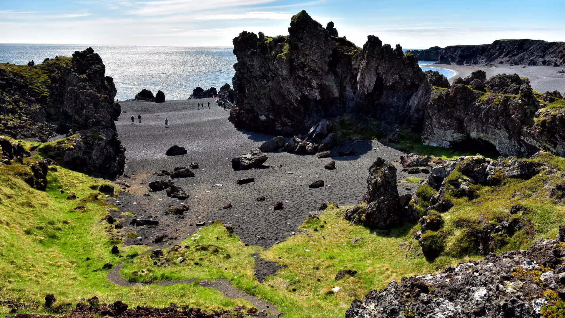 Black sand beach with dramatic volcanic rock formations and visitors on Snaefellsnes Peninsula, Iceland