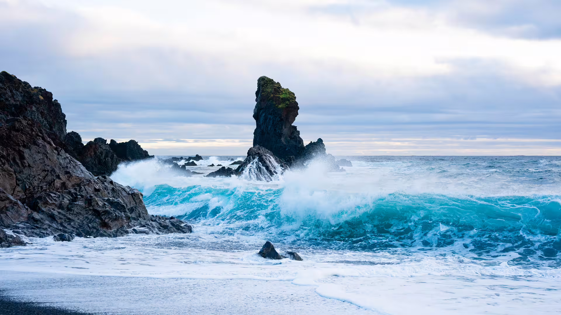 Dramatic crashing turquoise waves against black volcanic rock sea stack on Snaefellsnes Peninsula Iceland