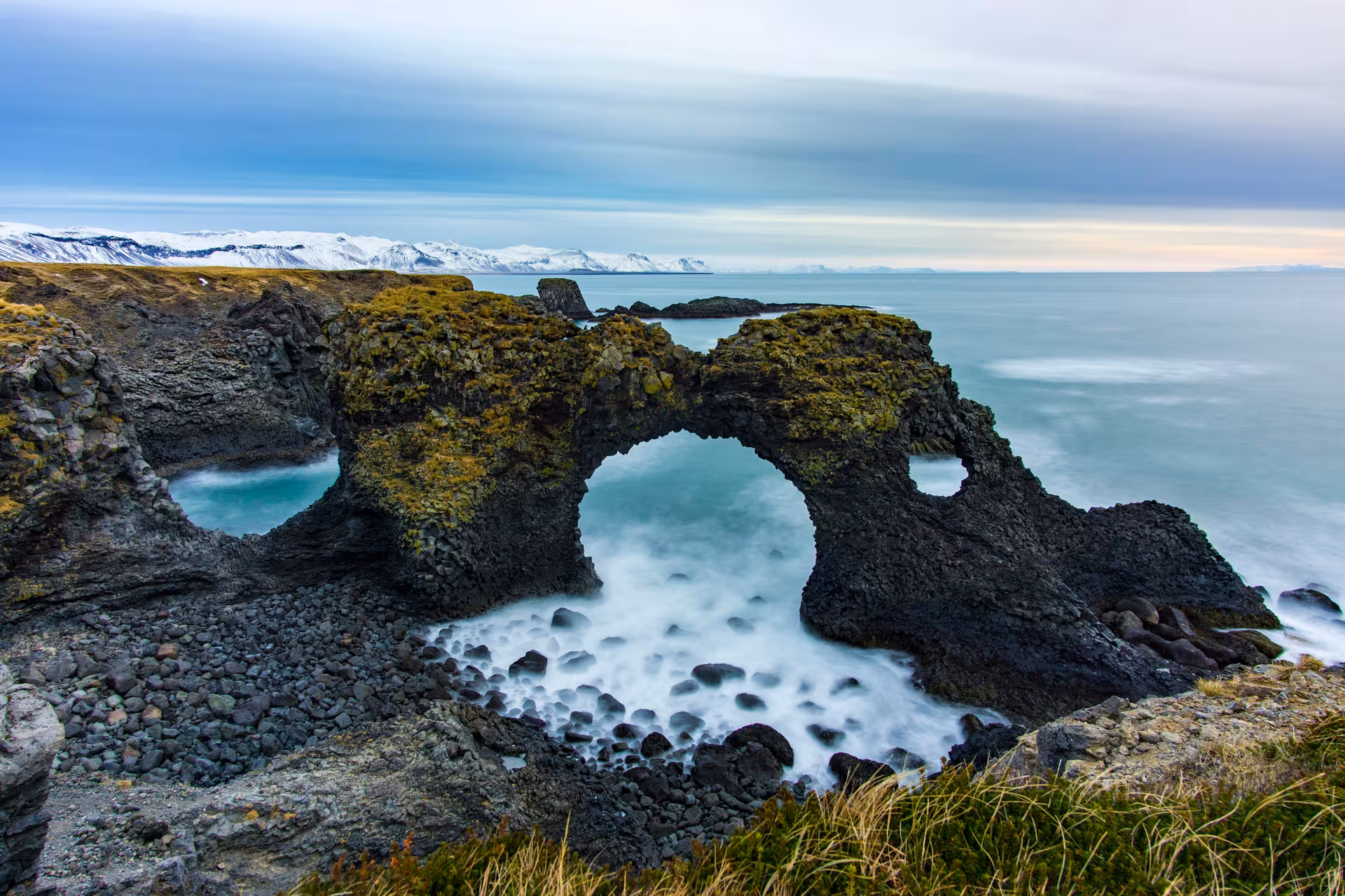 Gatklettur rock arch on Snaefellsnes Peninsula coastline with snow-capped mountains and misty ocean waves