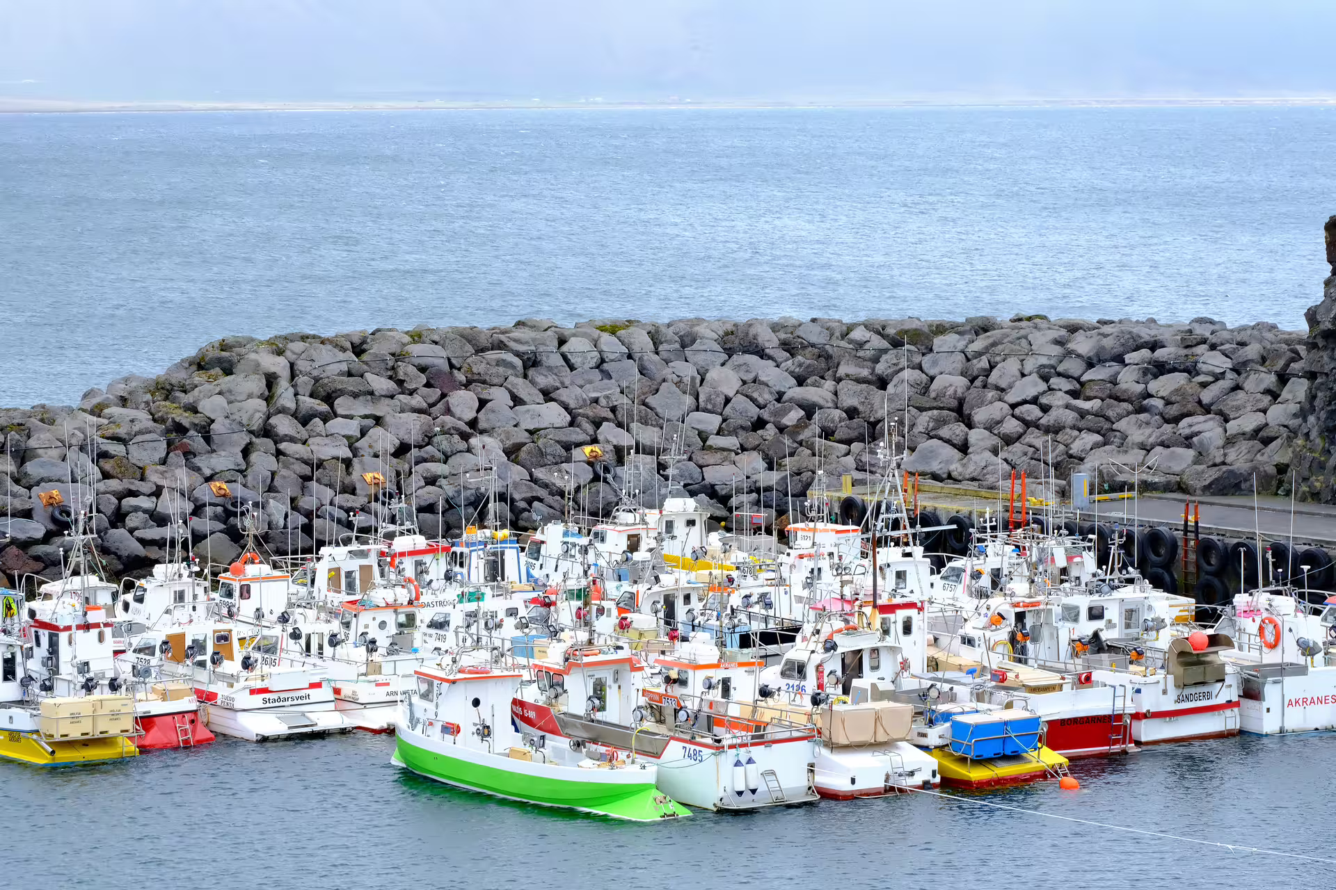 Colorful fishing boats docked at a small harbor with rocky breakwater in Snaefellsnes, Iceland