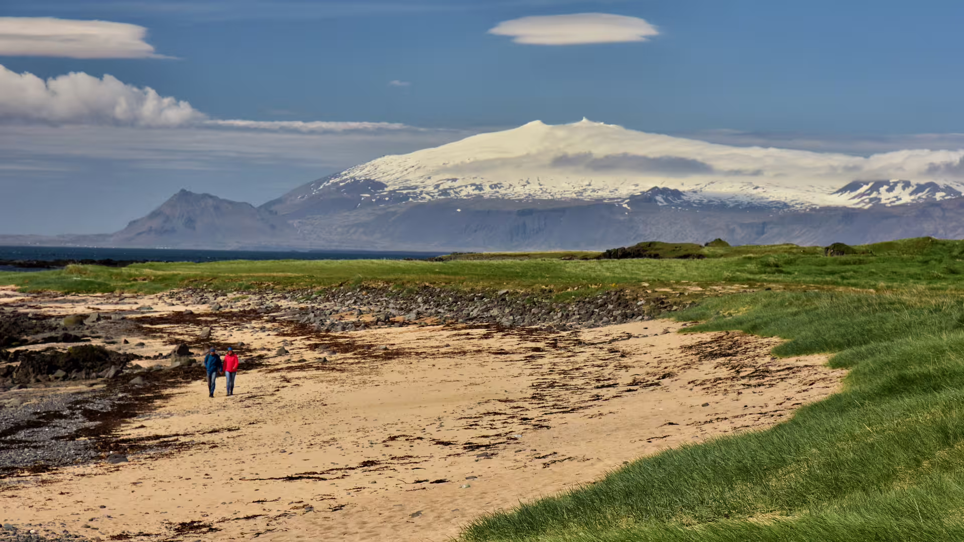 Couple walking on black sand beach with Snæfellsjökull glacier volcano in background, Iceland