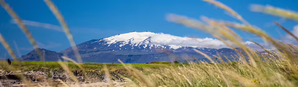 Snow-capped Snæfellsjökull glacier volcano rising above green fields under a blue sky in Iceland