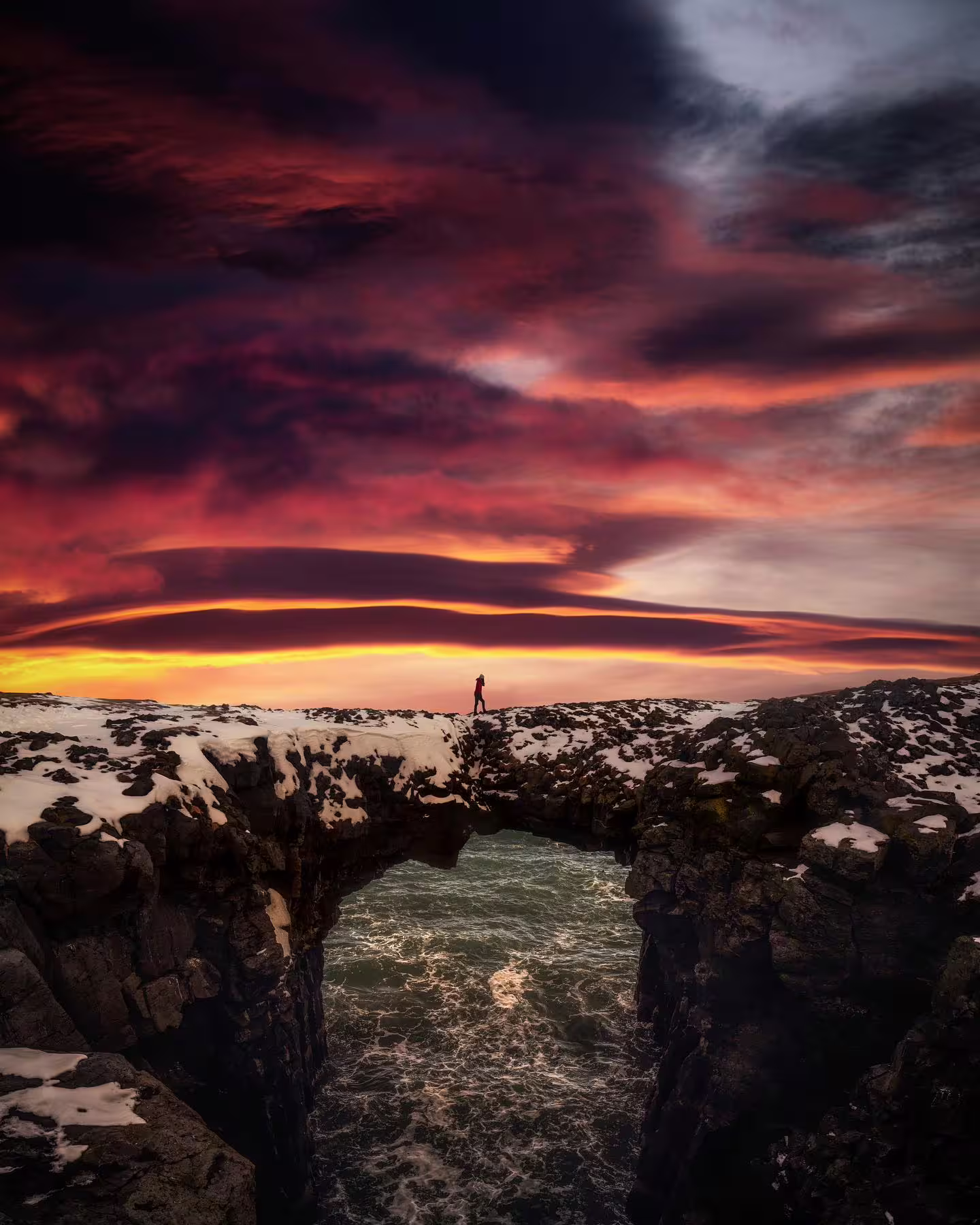 Solo hiker silhouetted on snowy lava rock arch at fiery sunset on Snaefellsnes hidden gem west Iceland