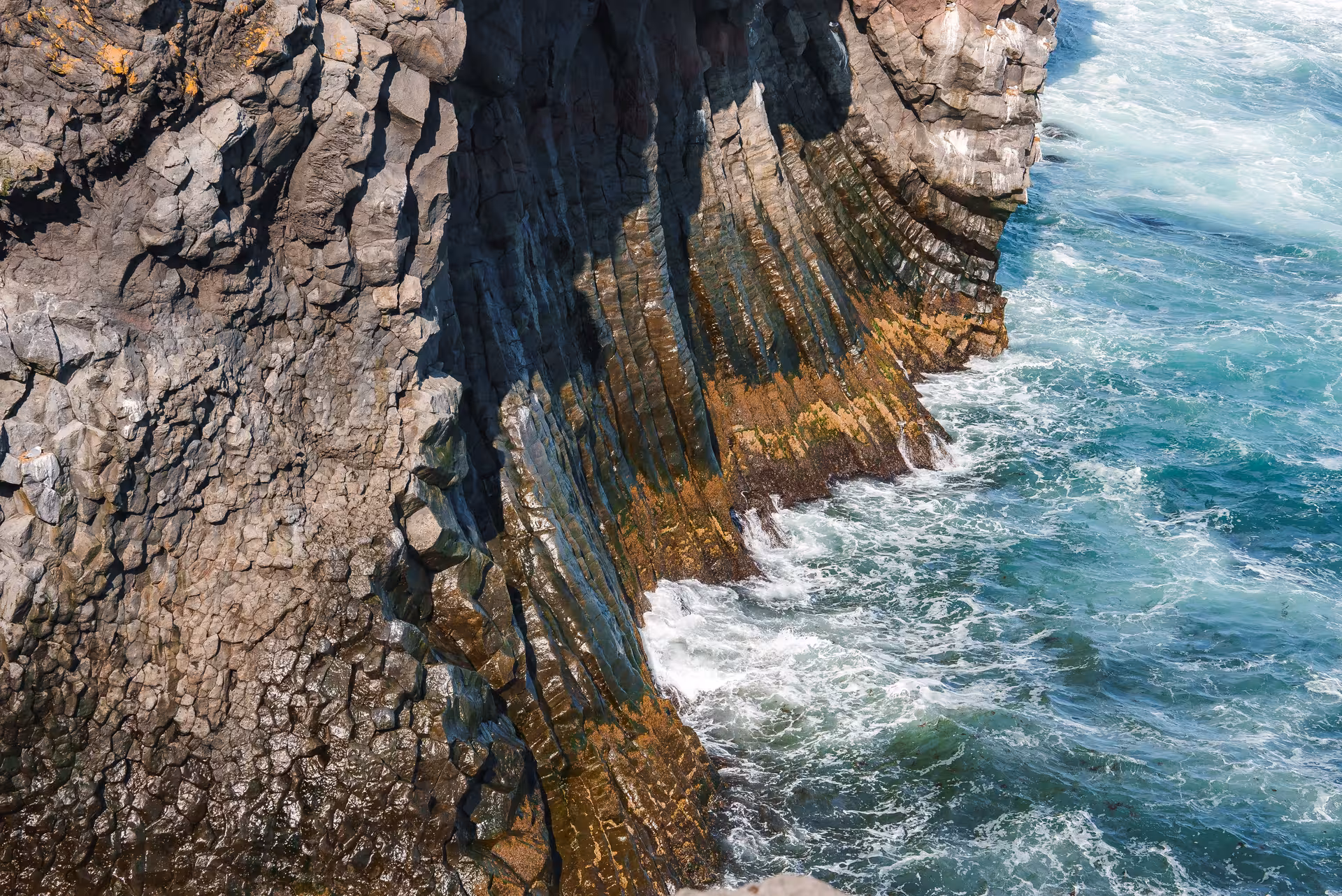 Dramatic basalt cliff columns meeting turquoise ocean waves on Snaefellsnes Peninsula coastline