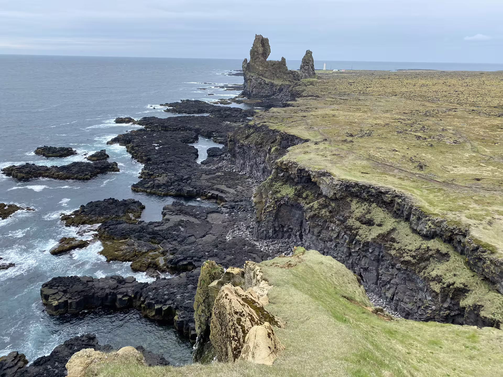 Dramatic basalt lava coastline cliffs and sea stacks at Snaefellsnes Peninsula Iceland with lighthouse in distance