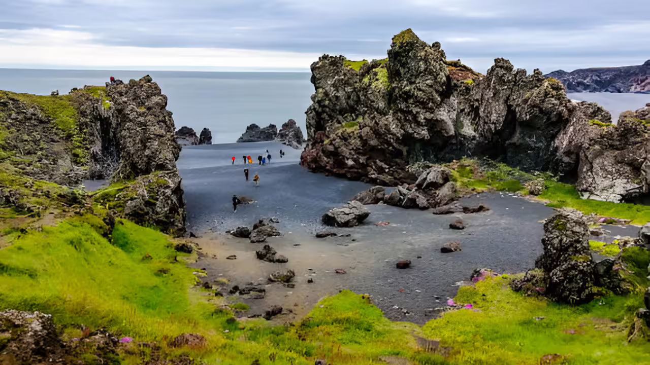 Black sand beach with lava rock formations and tourists exploring Snaefellsnes Peninsula coastline, Iceland