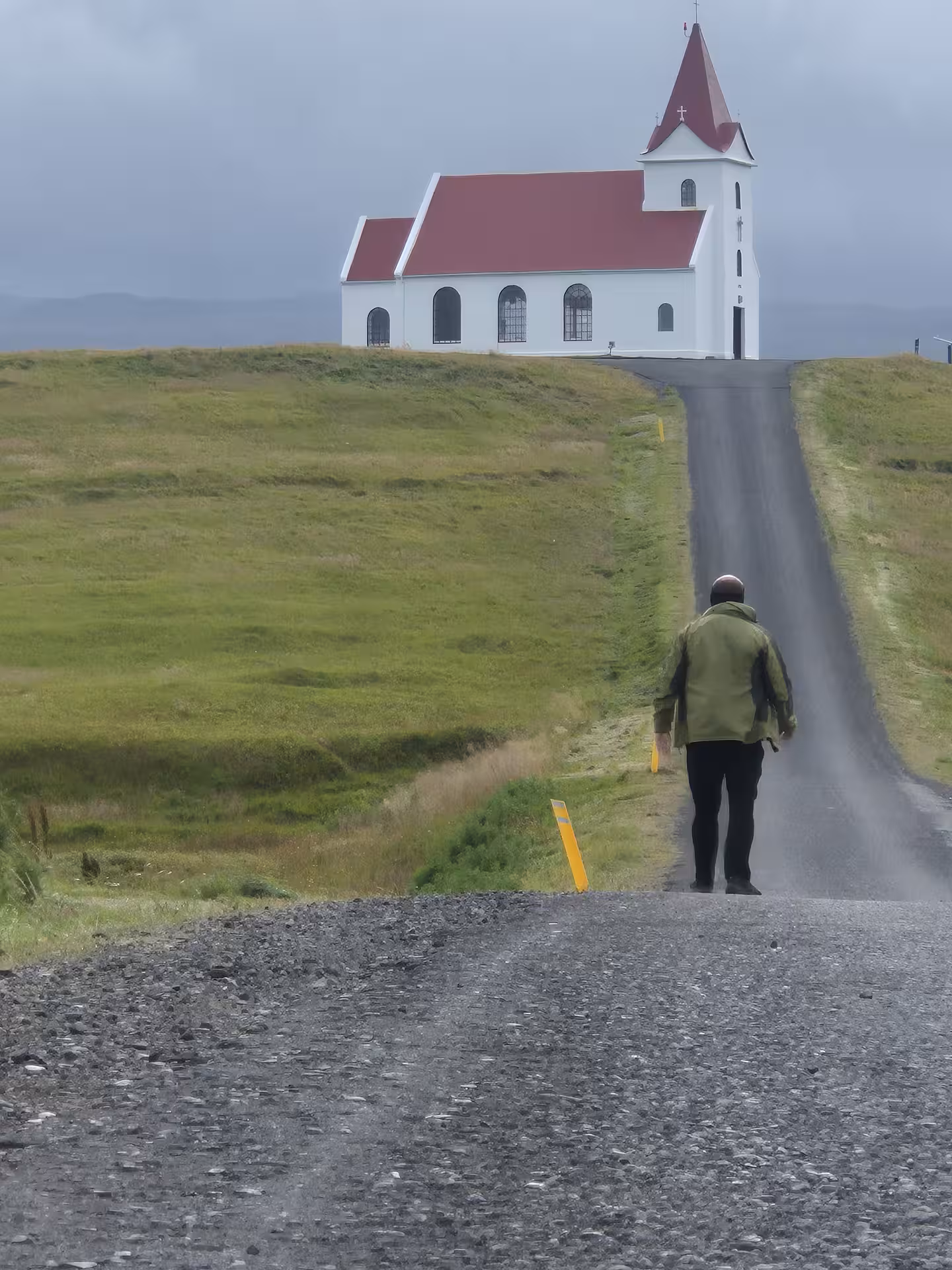 Man walking up narrow road toward white church with red roof on Snaefellsnes Peninsula, Iceland