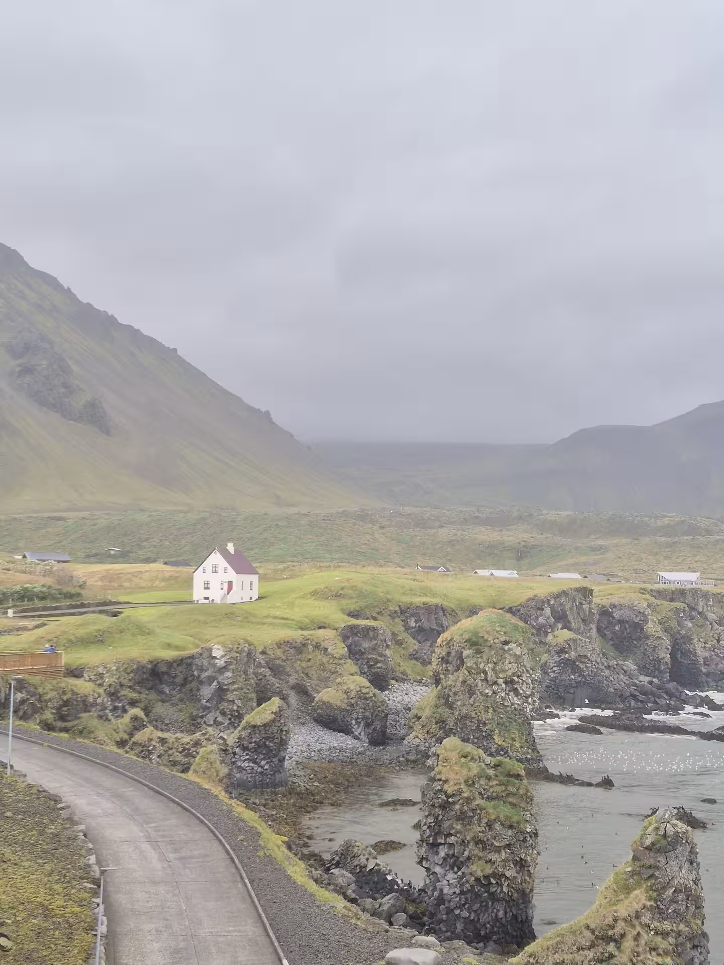 Lone white house with red roof on coastal cliffs with green mountains in Snaefellsnes Peninsula, Iceland