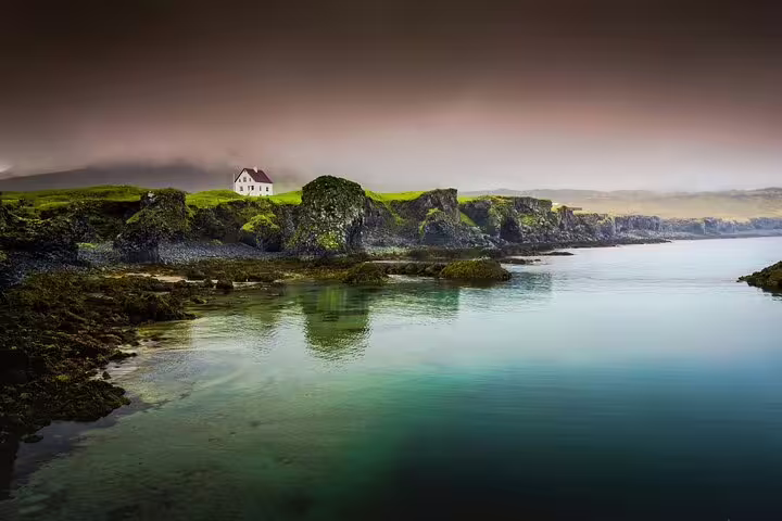 Mossy coastal cliffs with lone white house overlooking tranquil turquoise waters on Snaefellsnes Peninsula, Iceland