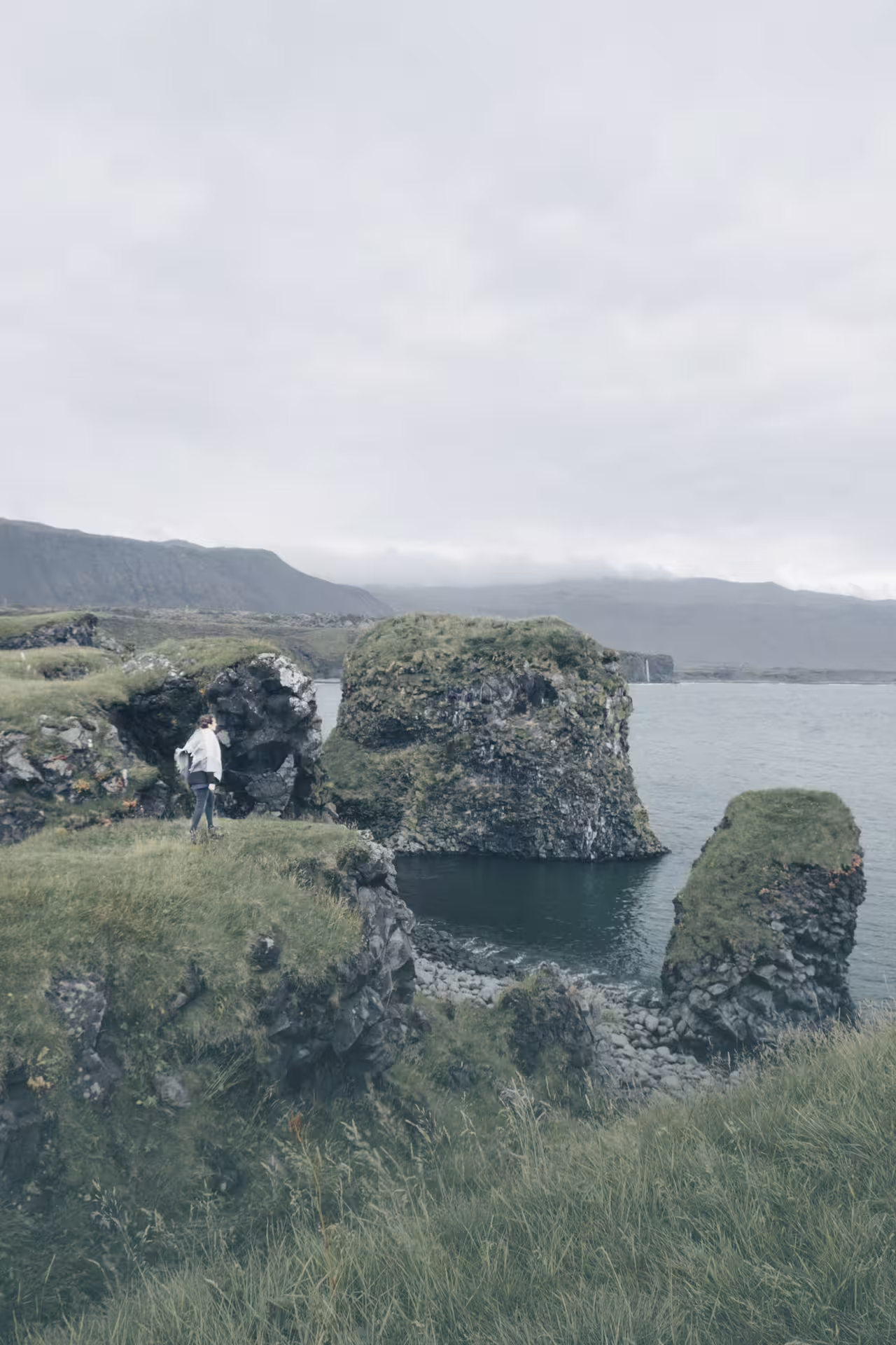 Hiker exploring mossy sea cliffs and rock arch on Iceland's Snæfellsnes Peninsula coastline