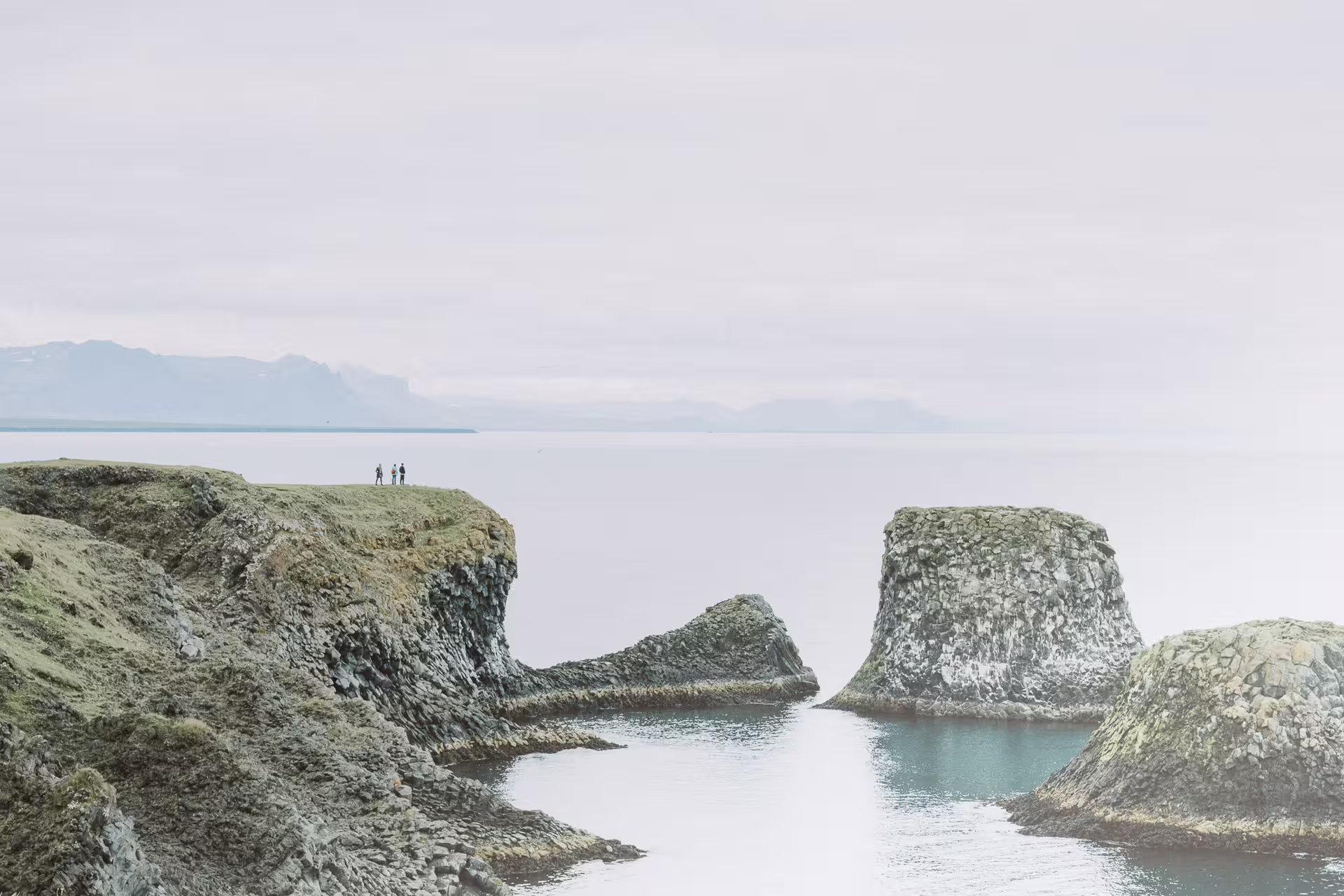 Rocky coastal cliffs and sea stacks of Snaefellsnes Peninsula with hikers standing on cliff edge
