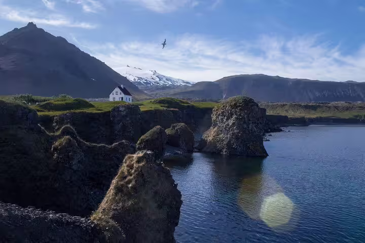 Rocky coastal cliffs with white house and snow-capped Snæfellsjökull volcano on Snaefellsnes Peninsula, Iceland