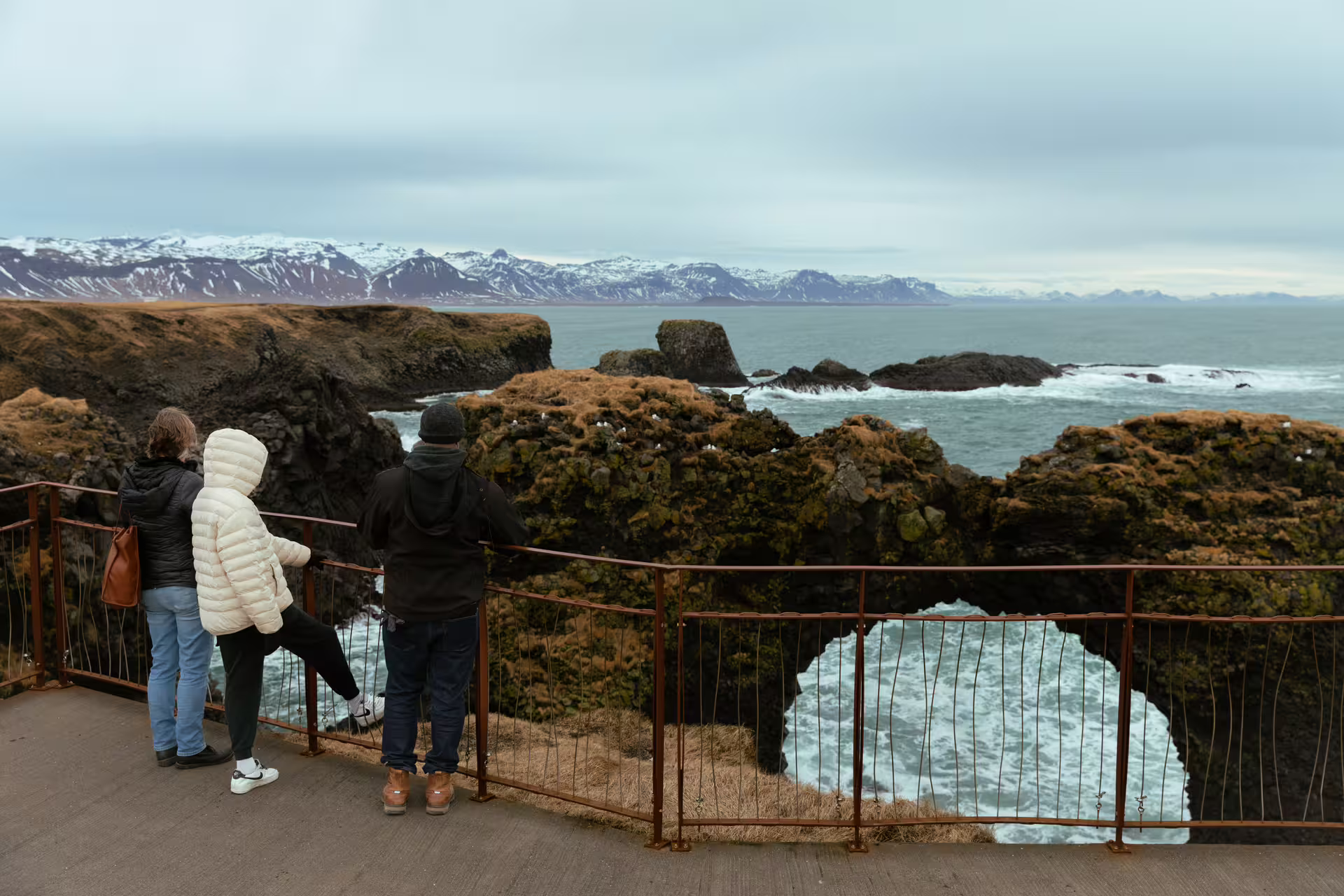 Tourists viewing rugged volcanic coastline and snow-capped mountains on Snaefellsnes Peninsula, Iceland