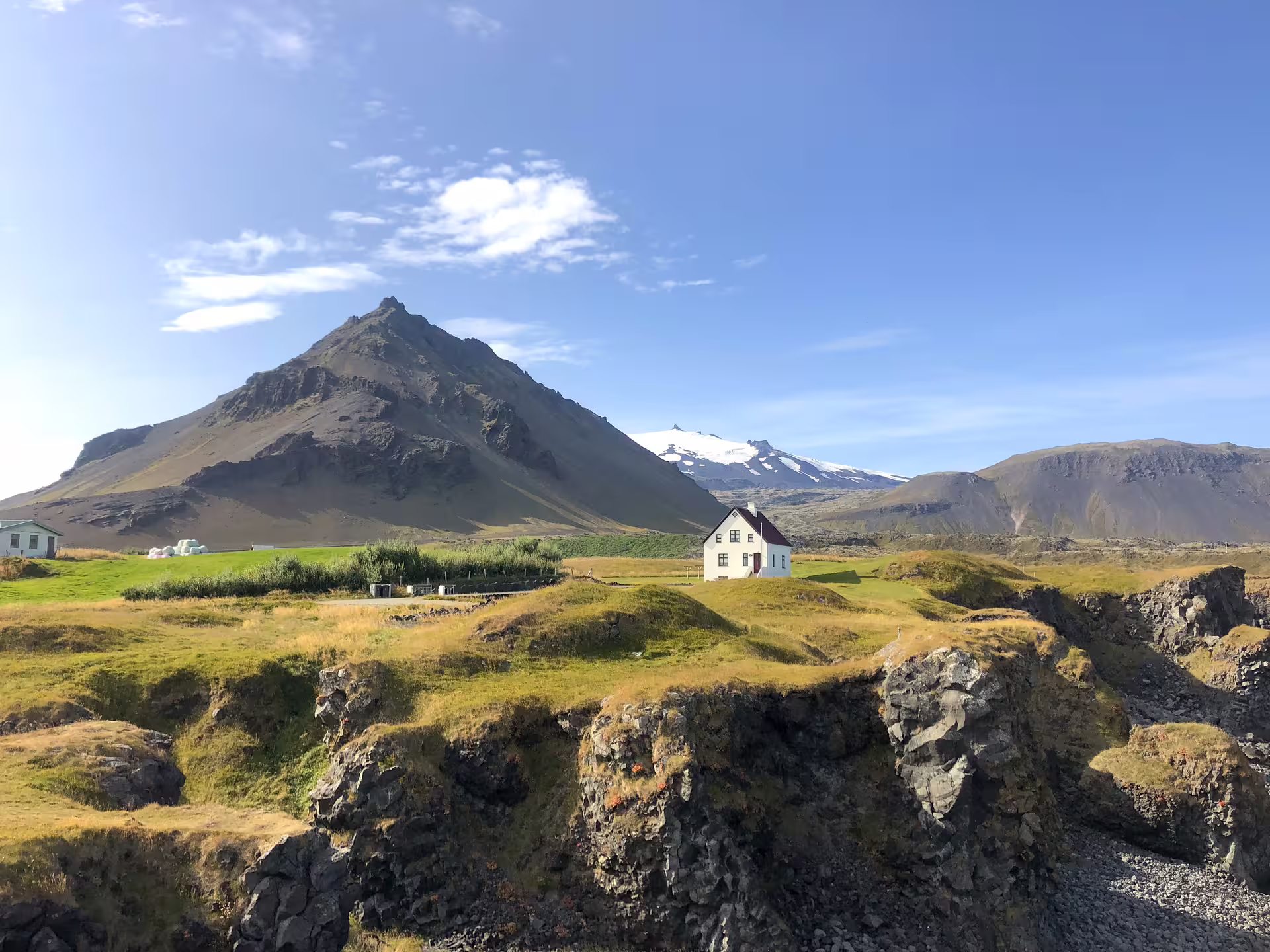 Lone white farmhouse on Snaefellsnes Peninsula with volcanic peak and glaciated Snæfellsjökull in background