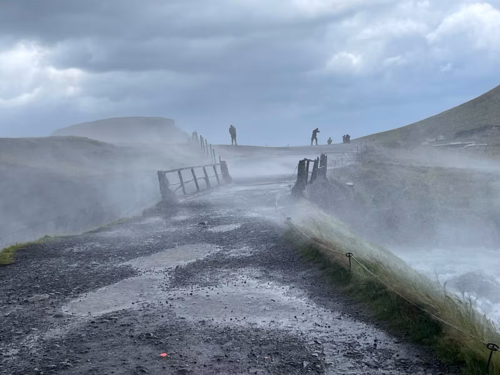 Steaming geothermal vents along misty trail on Snaefellsnes Peninsula with silhouetted visitors on ridge