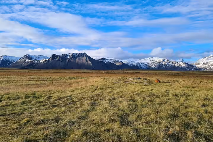 Vast green grasslands with snow-capped mountains under blue skies on Snaefellsnes Peninsula, Iceland