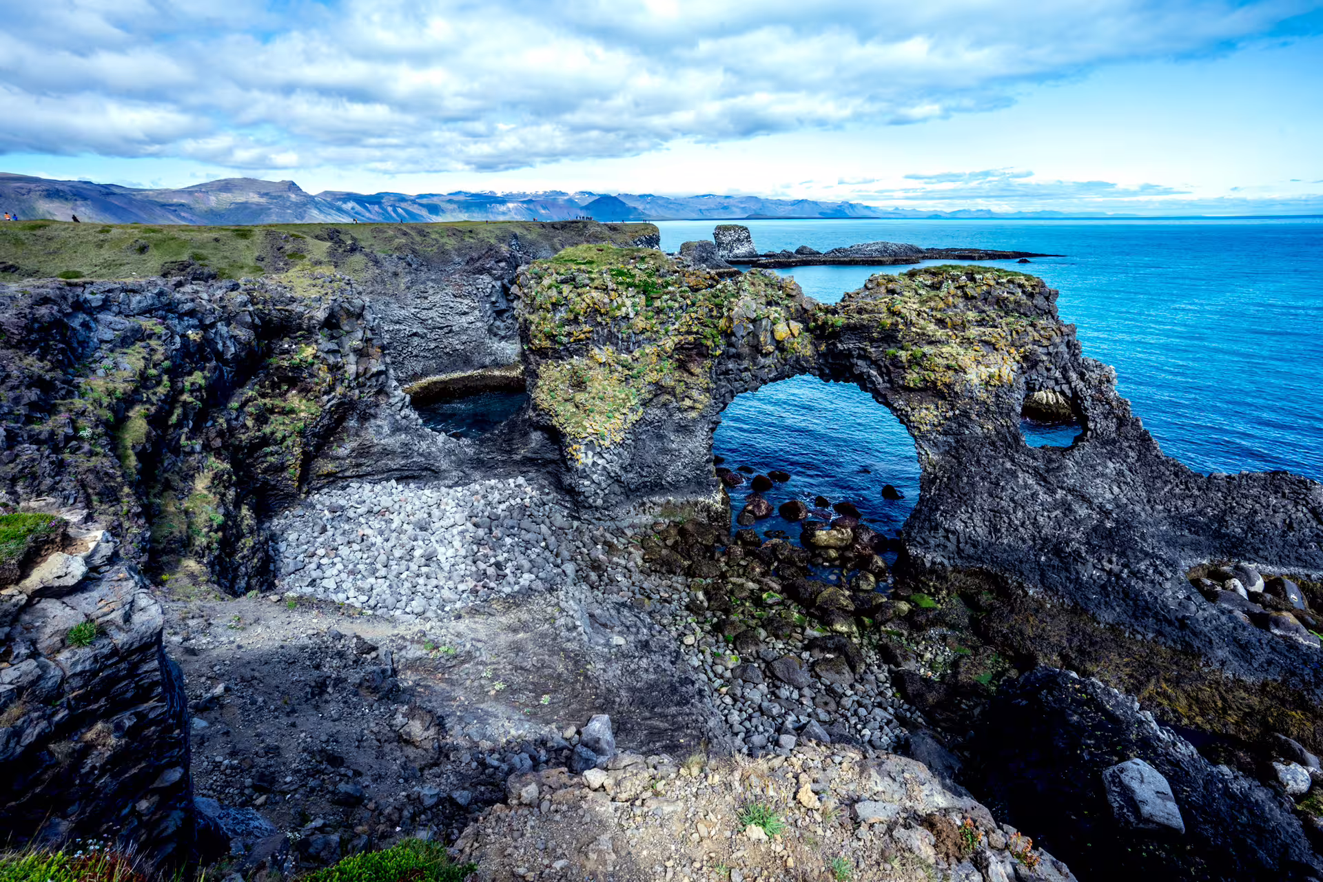 Natural lava rock arch on Snaefellsnes Peninsula coastline with blue ocean and mountains in background