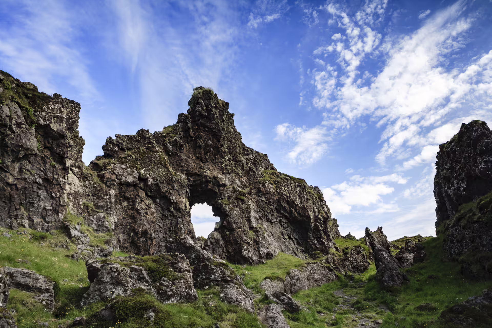 Rugged mossy lava rock formations with natural arch opening under blue sky on Snaefellsnes Peninsula Iceland