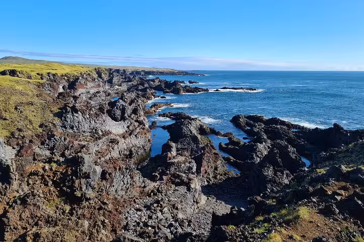 Rugged black lava rock coastline along Snaefellsnes Peninsula with blue ocean and green cliffs