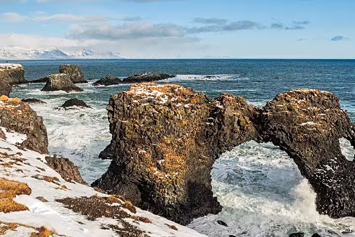 Rocky sea arch on Snaefellsnes Peninsula coastline with snow-dusted lava rocks and crashing waves