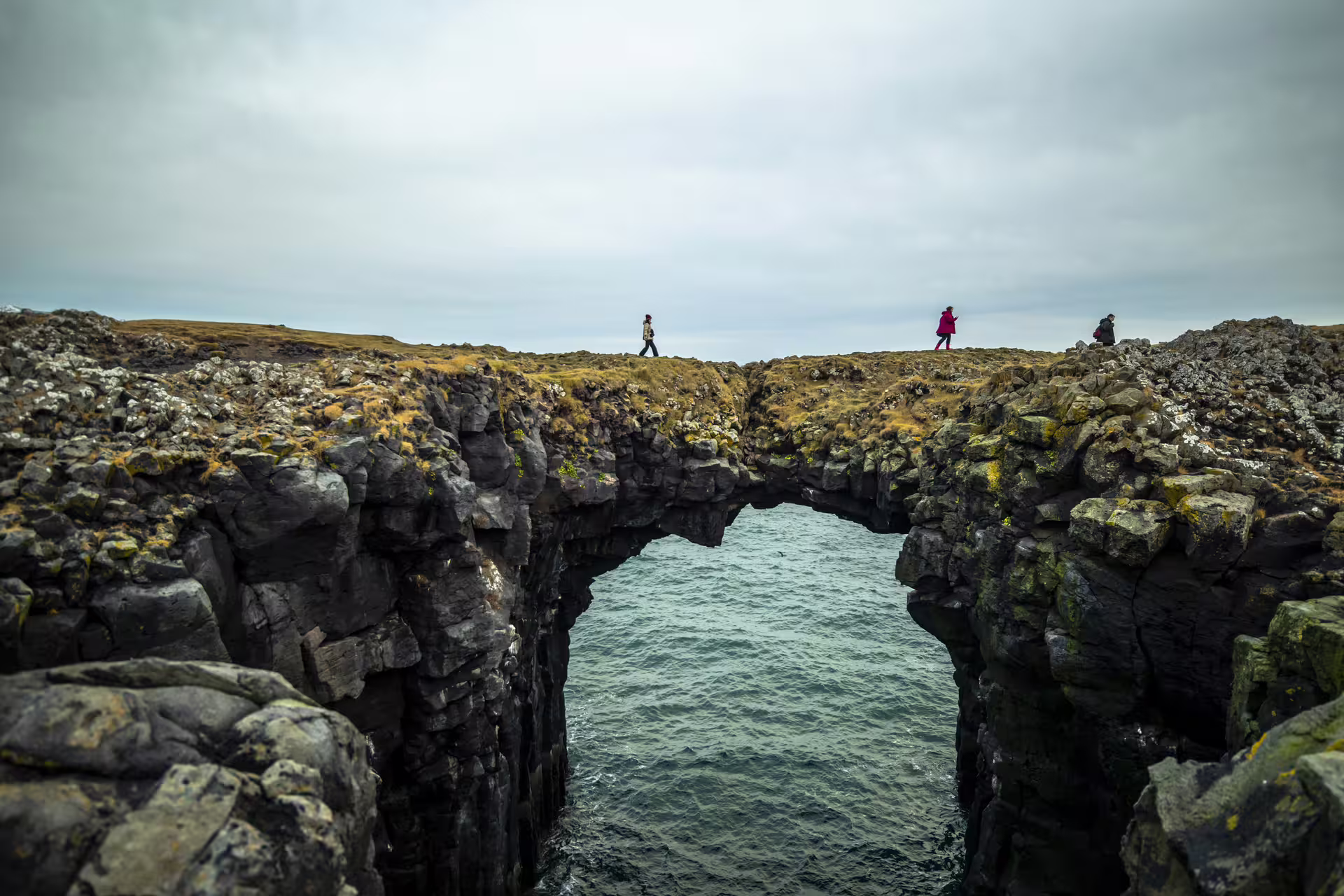 Natural rock arch bridge over ocean waters on the Snaefellsnes Peninsula, Iceland, with tourists walking nearby