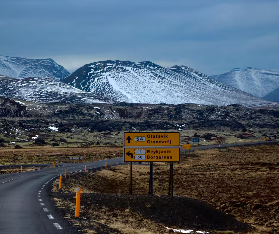 Yellow road signs pointing to Reykjavík and Ólafsvík on Snaefellsnes Peninsula with snow-capped mountains