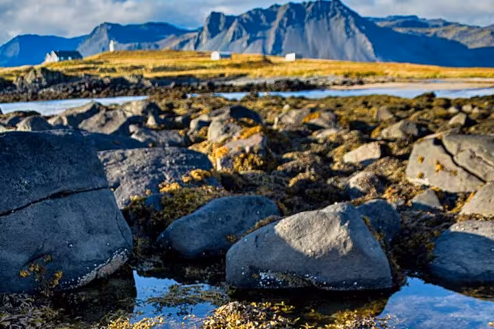 Rocky volcanic coastline with white farmhouses and dramatic mountains in Snaefellsnes Peninsula, West Iceland