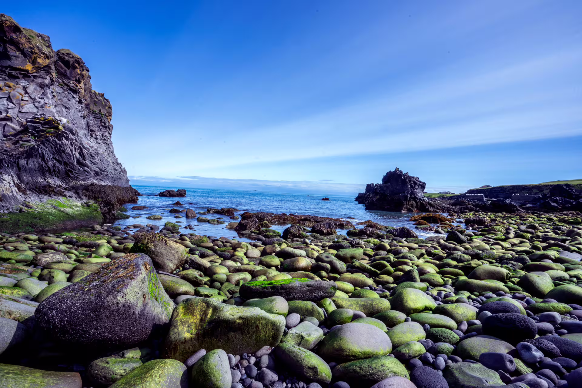 Mossy green boulders on a rocky shoreline with sea stacks and blue ocean at Snaefellsnes Peninsula