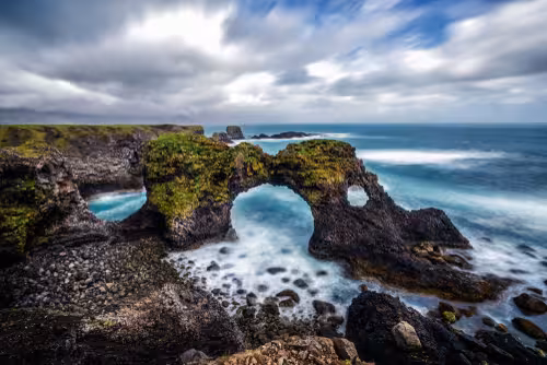 Rocky sea arch on Snaefellsnes Peninsula coastline with mossy cliffs and blue ocean waves