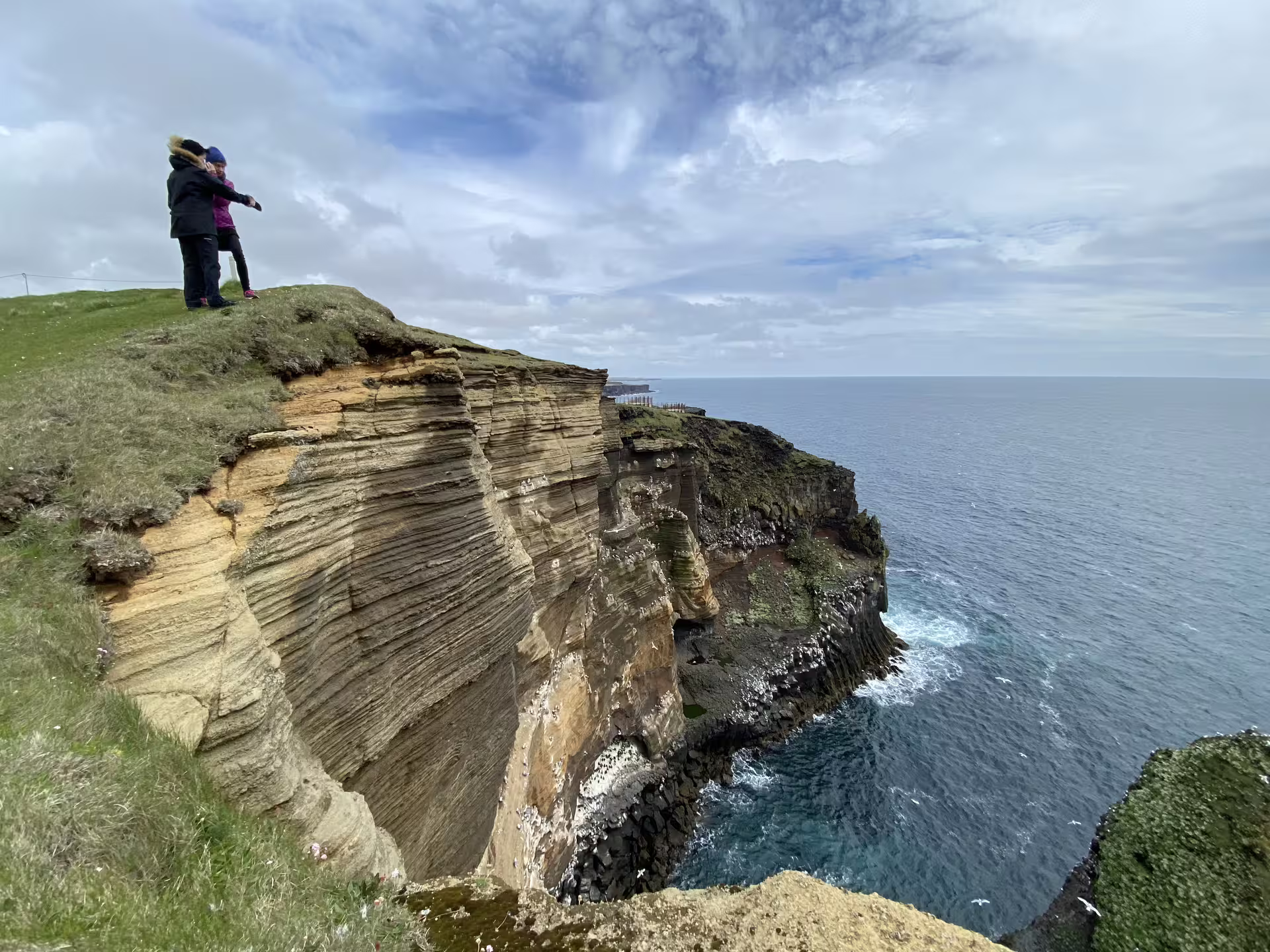 Two visitors standing on dramatic layered sea cliffs overlooking the Atlantic Ocean on Snaefellsnes Peninsula, Iceland