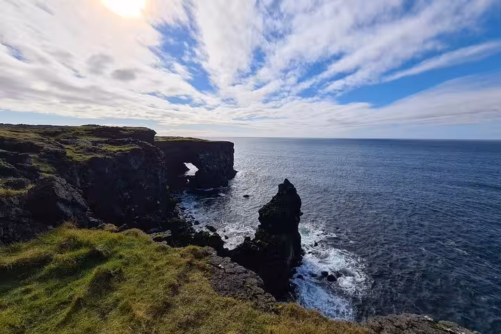 Rocky sea cliffs with natural arch on Snaefellsnes Peninsula coastline under cloudy blue sky