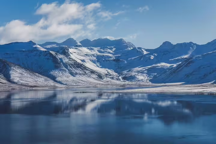 Snow-capped mountains of Snaefellsnes Peninsula reflected in calm glacial lake under blue sky