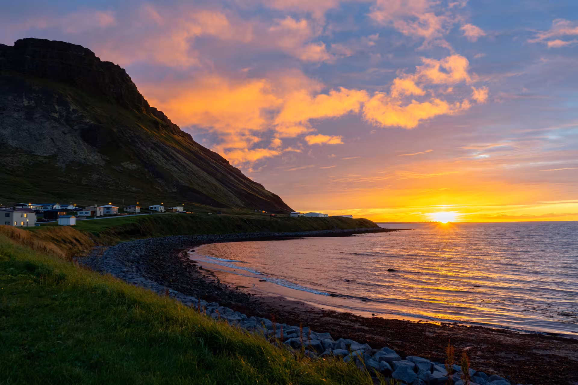 Sunset over a curved black sand beach with a small coastal village and dramatic mountain on the Snaefellsnes Peninsula, Iceland