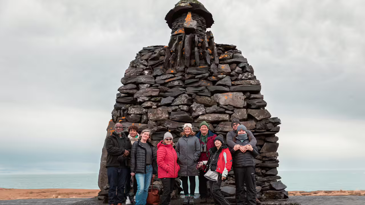 Group of tourists posing in front of large lava rock cairn sculpture on Snaefellsnes Peninsula, Iceland