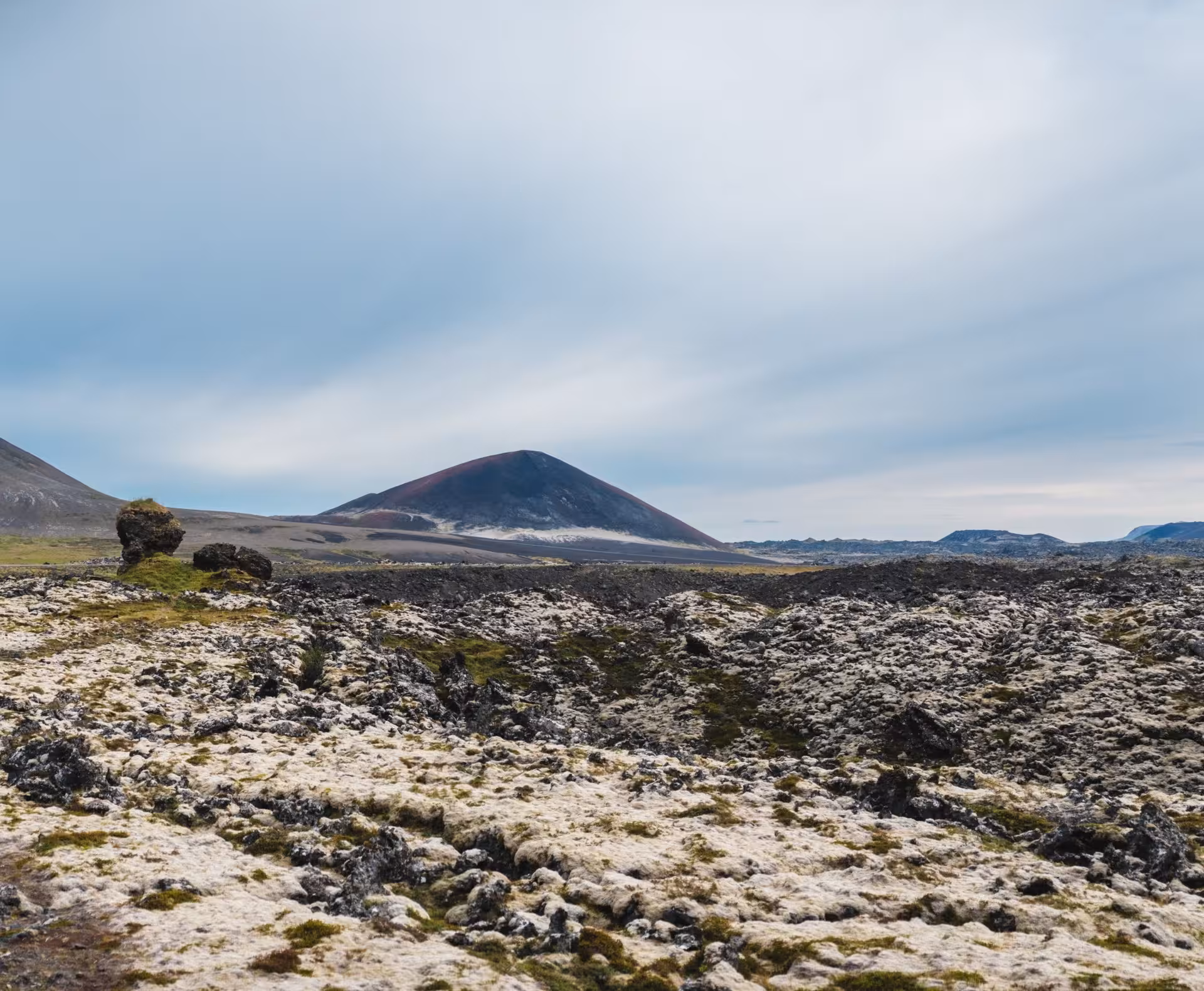 Volcanic lava field with mossy rocks and a dark cinder cone volcano on Snaefellsnes Peninsula, Iceland