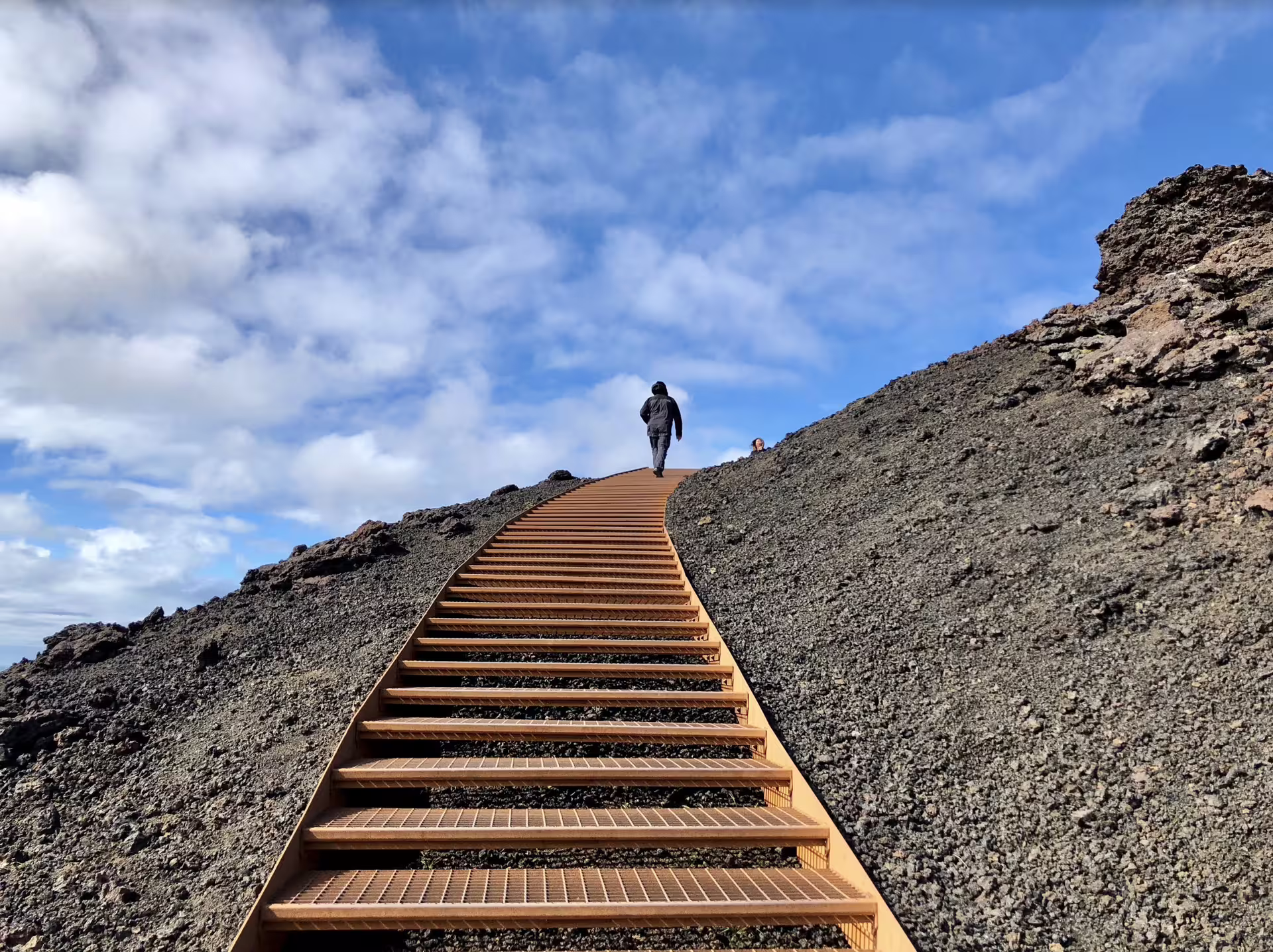 Hiker climbing steep wooden stairs up volcanic lava slope on Snaefellsnes Peninsula, Iceland