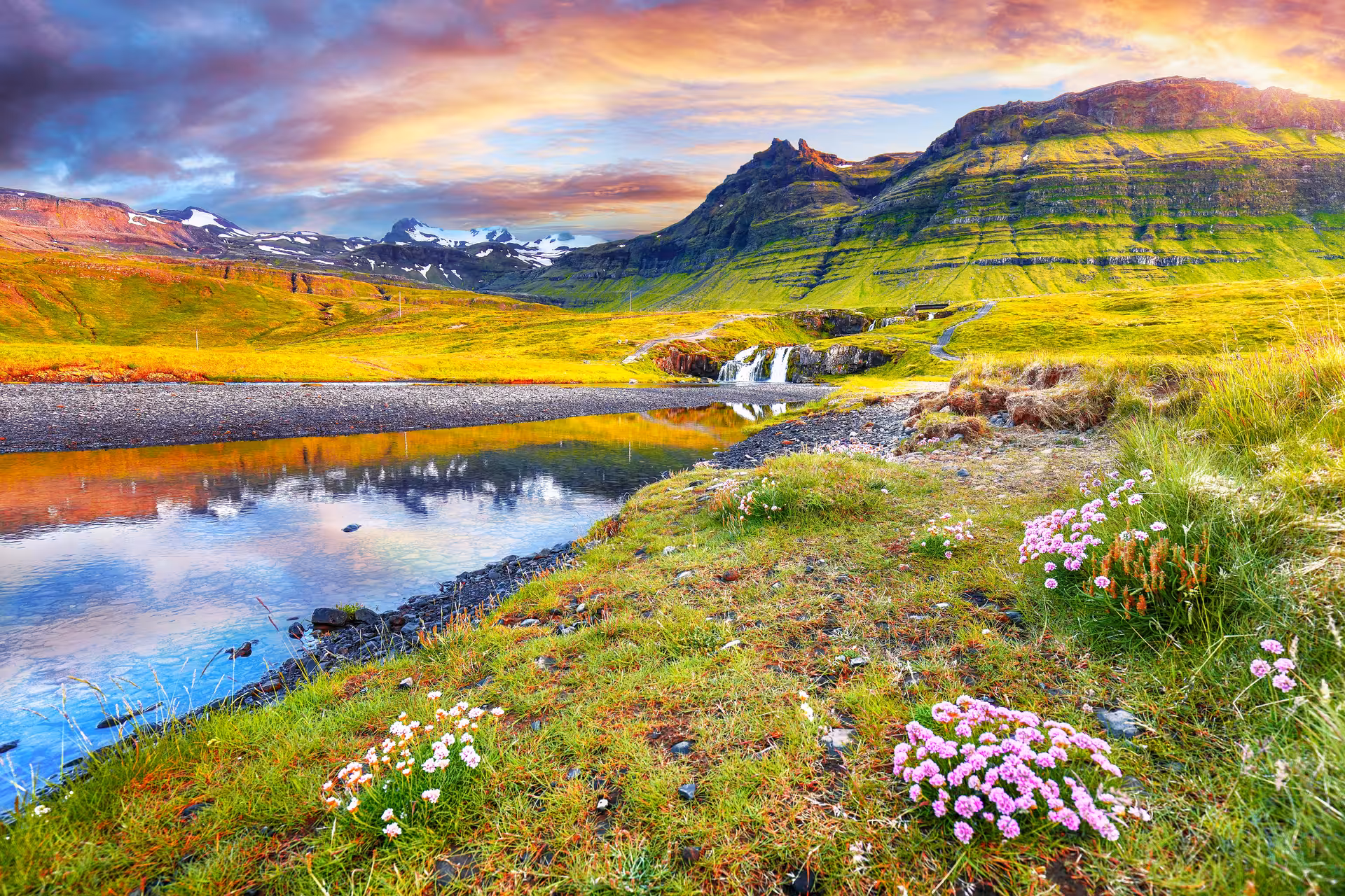 Scenic Snaefellsnes Peninsula landscape with green mountains, waterfall, river, and pink wildflowers at sunset