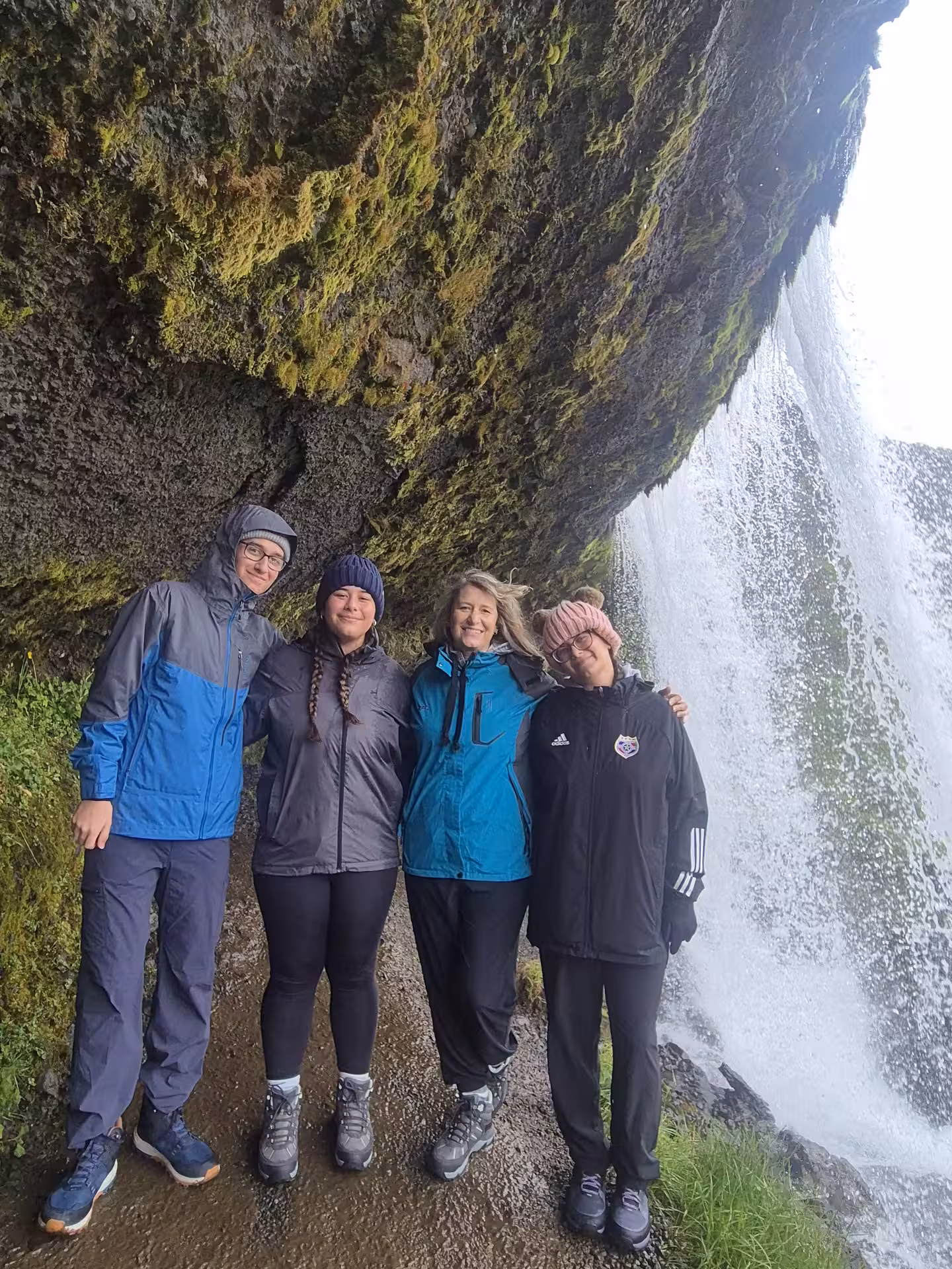 Four hikers posing behind a waterfall on the Snaefellsnes Peninsula, Iceland, wearing rain gear