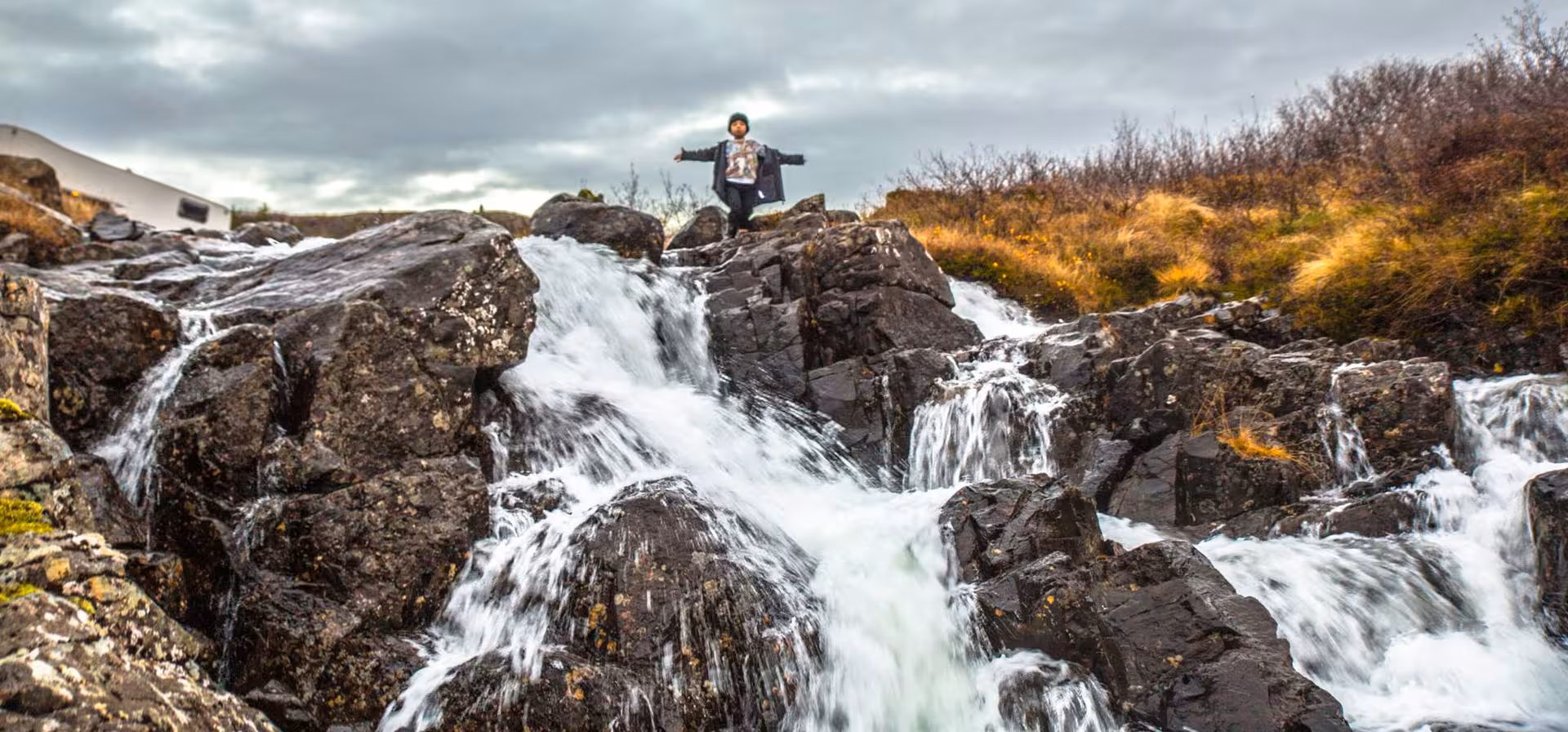 Traveler standing arms outstretched on rocky waterfall during Snaefellsnes Peninsula full-day tour
